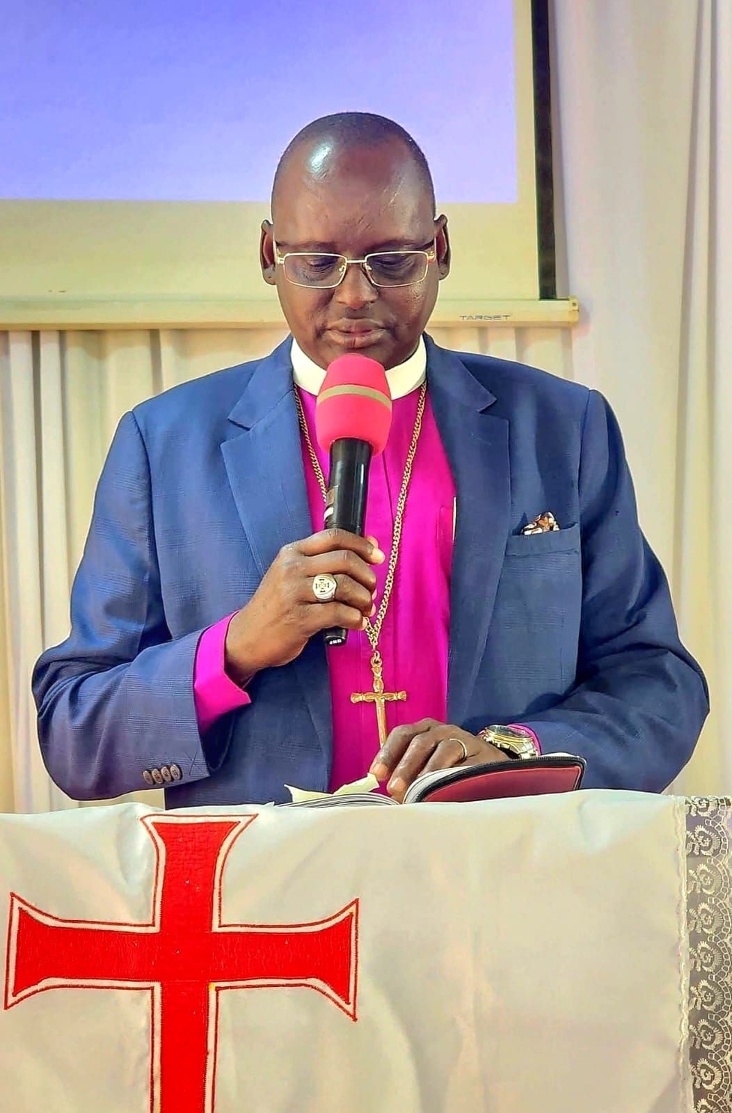 Bishop preaching at a lectern draped with a red cross